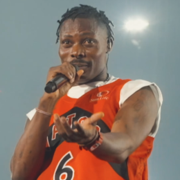 Asake in an orange Raptors jersey singing into a microphone on stage in Toronto