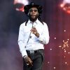 Burna Boy performing live in a white western shirt and black cowboy hat on stage