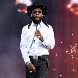 Burna Boy performing live in a white western shirt and black cowboy hat on stage