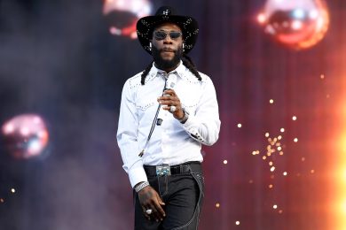 Burna Boy performing live in a white western shirt and black cowboy hat on stage
