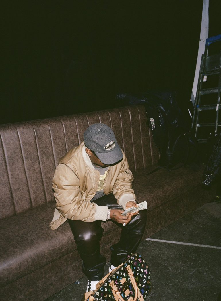 Asake counting cash in a Guess cap during the M$NEY era