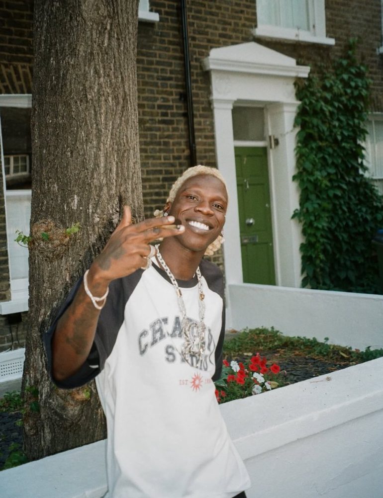 Seyi Vibez smiling outdoors in a Chase Studio shirt