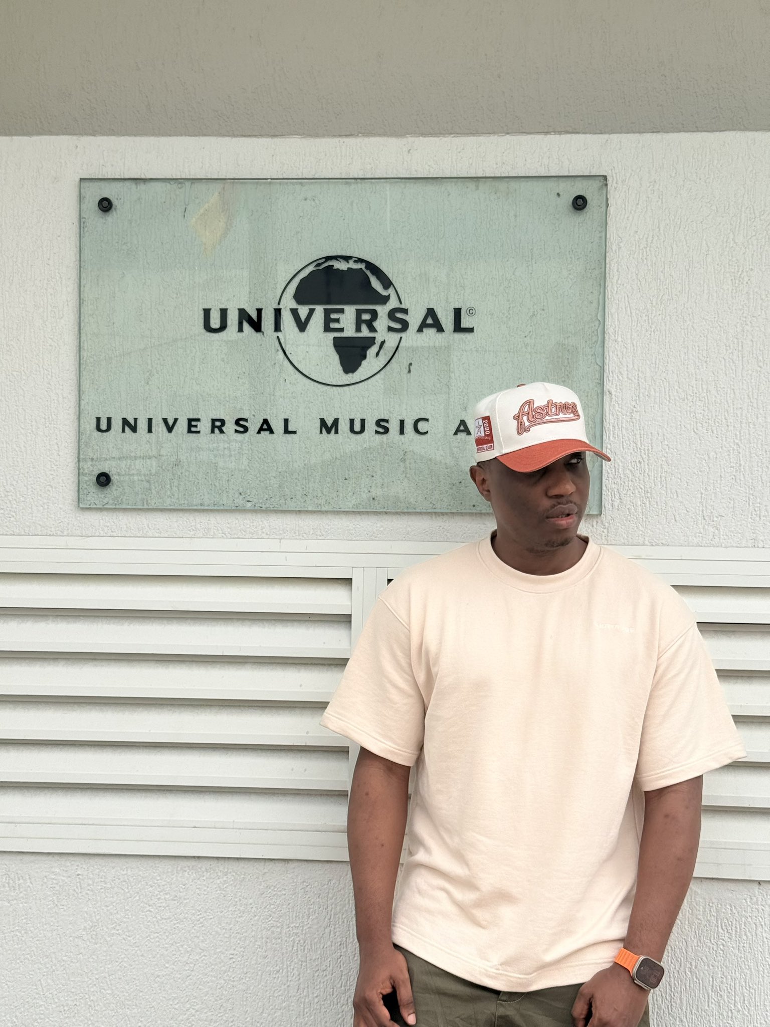 A-Q (Gilbert Bani) standing outside Universal Music Africa in a cream T-shirt and cap.