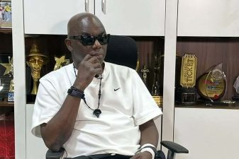 Headies founder Ayo Animashaun seated in his office in front of award trophies.