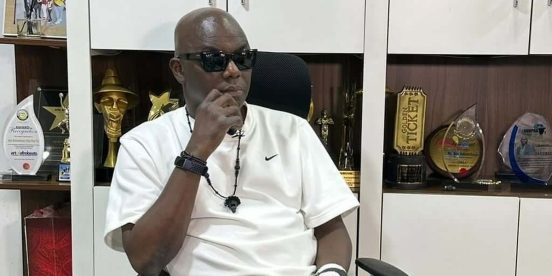 Headies founder Ayo Animashaun seated in his office in front of award trophies.