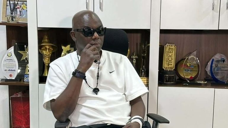 Headies founder Ayo Animashaun seated in his office in front of award trophies.