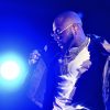 Davido performing on stage in a 001 chain and white T-shirt under blue lights at Reggae Geel in 2022