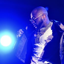 Davido performing on stage in a 001 chain and white T-shirt under blue lights at Reggae Geel in 2022