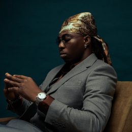 FOLA seated in a grey suit, looking down at his hands
