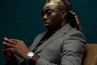 FOLA seated in a grey suit, looking down at his hands