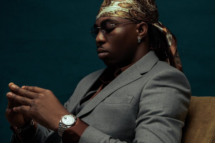 FOLA seated in a grey suit, looking down at his hands