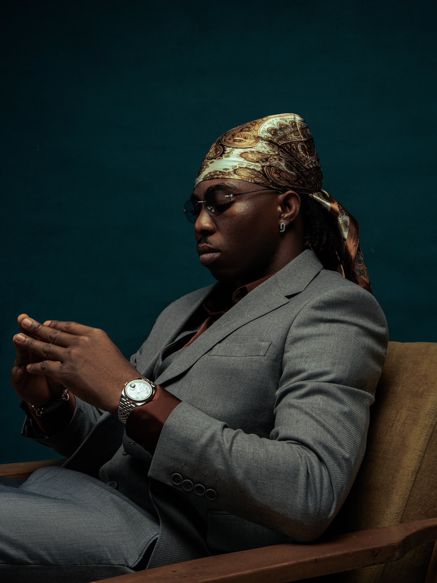 FOLA seated in a grey suit, looking down at his hands