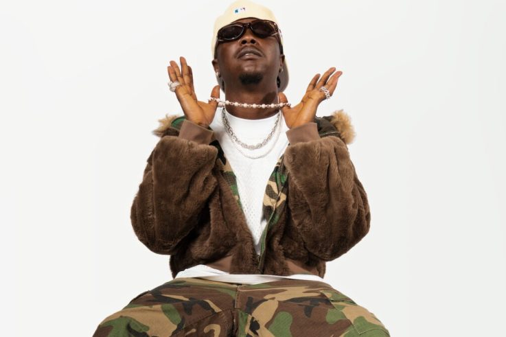 Magicsticks in a camouflage jacket and cream cap, hands raised