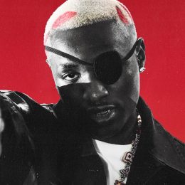 Ruger in a black eye patch and leather jacket, pointing at the camera against a red background