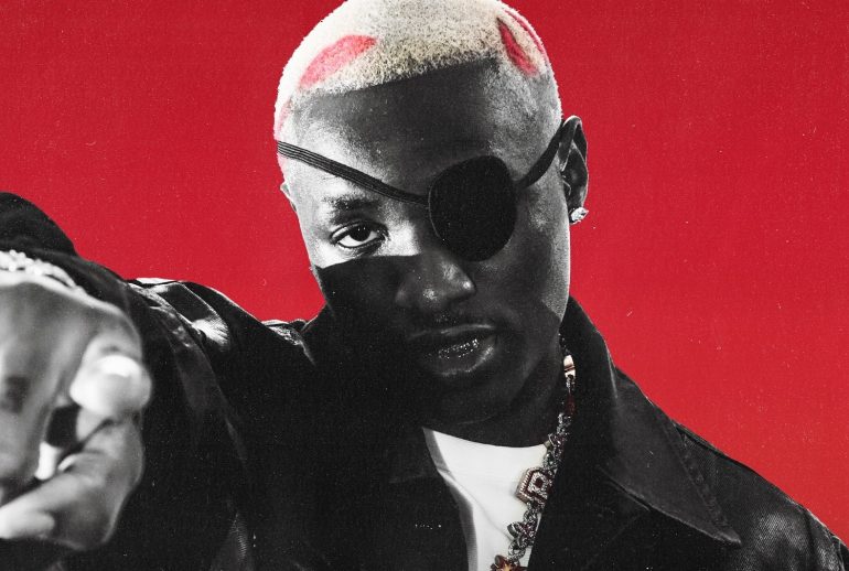 Ruger in a black eye patch and leather jacket, pointing at the camera against a red background