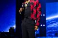 Wizkid on stage in a red plaid jacket holding a microphone at the Canex concert in Algiers