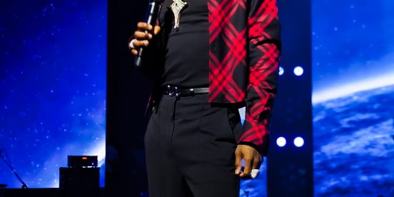 Wizkid on stage in a red plaid jacket holding a microphone at the Canex concert in Algiers