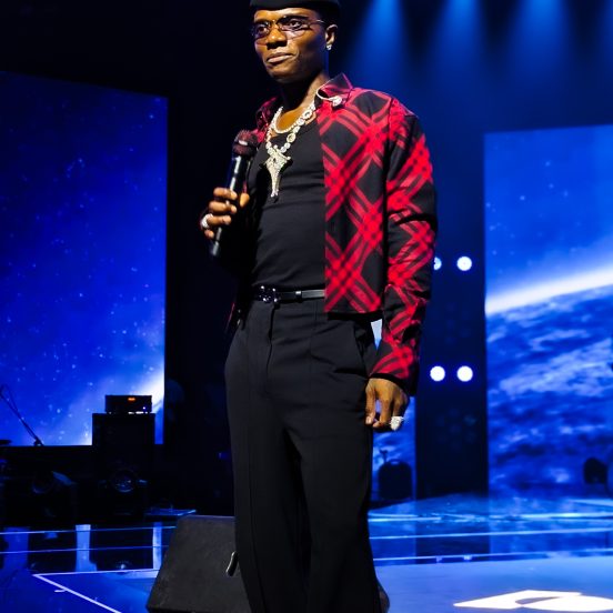 Wizkid on stage in a red plaid jacket holding a microphone at the Canex concert in Algiers